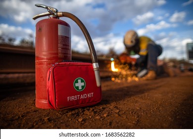 Safe workplace red First Aid Kit together with fire extinguisher are set ready in cases fire occurs with defocused construction worker conducting hot work oxy cutting steel plate structure background 