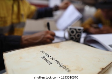 Safe Workplace Working At Heights Permit Book Placing On The Table With Defocused Construction Workers Writing And Organising Job Hazard Analysis Risk Assessment With Teammate Prior Starting Each Job 