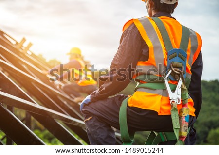 [safety body construction] Working at height equipment. Fall arrestor device for worker with hooks for safety body harness on selective focus. Worker as in construction background.