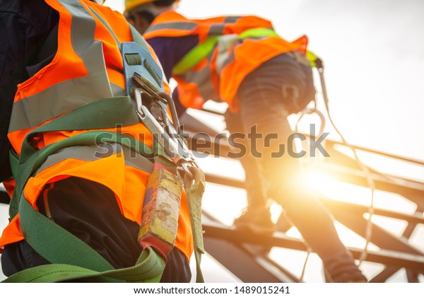 [safety body\
construction] Working at height equipment. Fall arrestor device for\
worker with hooks for safety body harness on selective focus.\
Worker as in construction\
background.