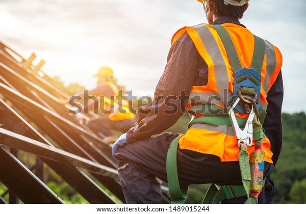 [safety body
construction] Working at height equipment. Fall arrestor device for
worker with hooks for safety body harness on selective focus.
Worker as in construction
background.
