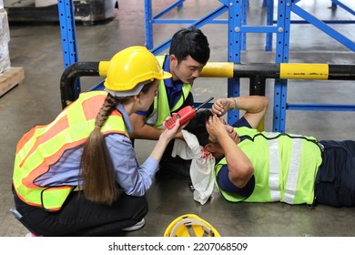 Safety Colleagues Team Helping Middle Aged Warehouse Asian Worker Who Had Broken Head Accident And Lying On The Floor In Warehouse While Using Walkie Talkie Radio. First Aid Training Concept.