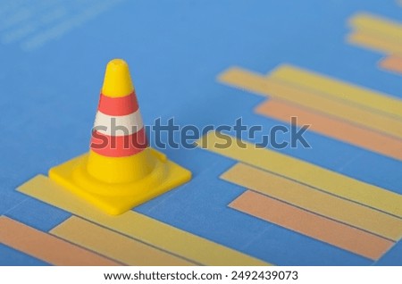 A safety cone alongside a fluctuating graph represents the need for caution and careful management in response to economic volatility and market uncertainties