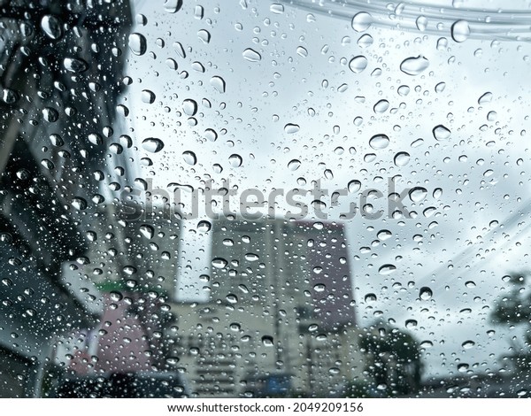 Safety driving car in rainy season concept. Rain\
drop falling in front of windshield window on road in heavy traffic\
in big city.