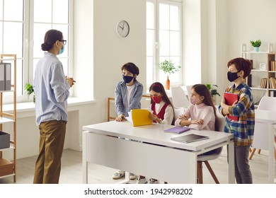 Safety Education, New Normal School After Coronavirus Quarantine Lockdown. Female Tutor Teaching Pupils Small Group In Classroom. Educator And Students Wearing Protective Medical Face Mask