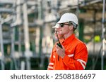 A safety engineer in an orange jumpsuit and white hard hat uses a radio to communicate at site, ensuring smooth operations. The image highlights the importance of safety communication in industrial.