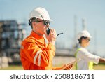 A safety engineer in an orange jumpsuit and white hard hat uses a radio to communicate at site, ensuring smooth operations. The image highlights the importance of safety communication in industrial.