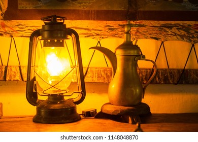 A Safety Fas Lamp With Electric Bulb Casts Light On A Old Style Tea Pot.