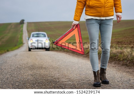 Safety first. Broken car on the road. Driver holding warning triangle. Misfortune on travel. Woman need roadside assistance after car accident