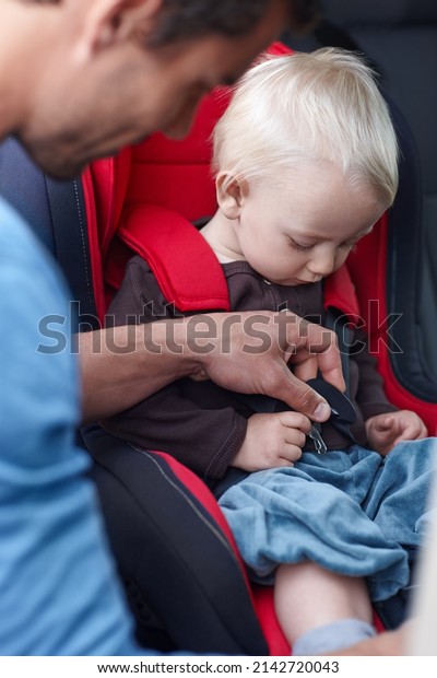 Safety first. A father helping his child in a baby\
seat for the car.