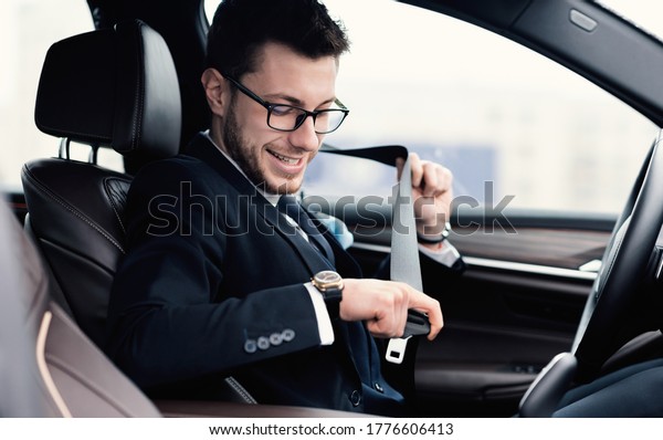 Safety First. Glad\
business man in eyewear fastening his seat belt, sitting in the\
luxury car, side view