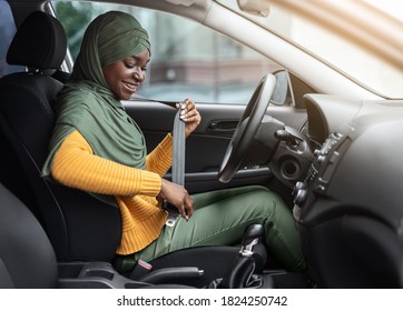 Safety First. Smiling Black Muslim Woman In Hijab Fastening Seatbelt In Her Car Before Driving In City, Following Safe Ride Rules, Ready For Travel With Auto, Side View With Free Space - Powered by Shutterstock