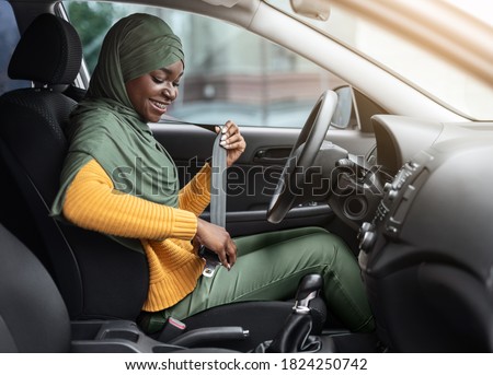 Safety First. Smiling Black Muslim Woman In Hijab Fastening Seatbelt In Her Car Before Driving In City, Following Safe Ride Rules, Ready For Travel With Auto, Side View With Free Space