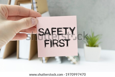 Safety first in unsafe workplace concept photo. Hand of staff is holding the text sign with blurred background of drilling rig or refinery plant equipment at worksite location.