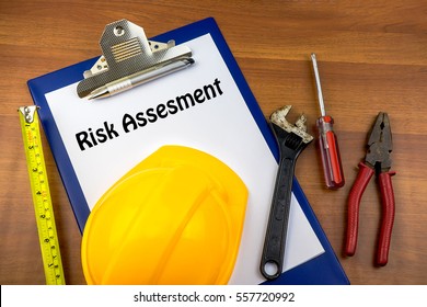 Safety Helmet, Pen And Hand Tools, Clip Board With Text Risk Assessment On Wooden Background. Construction Concept.