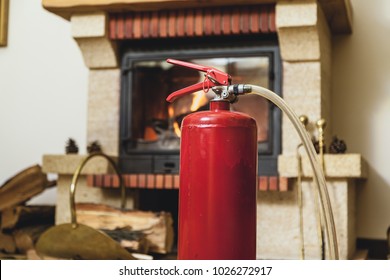 Safety At Home. Red Fire Extinguisher Stands In Front Of A Burning Fireplace In A Modern Interior
