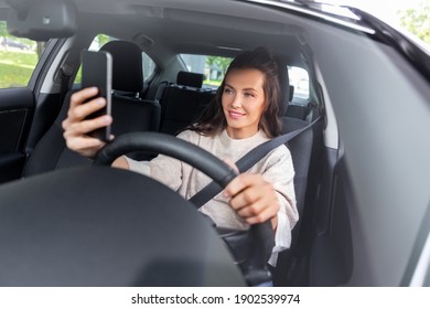 Safety And People Concept - Happy Smiling Young Woman Or Female Driver Driving Car And Taking Selfie With Smartphone