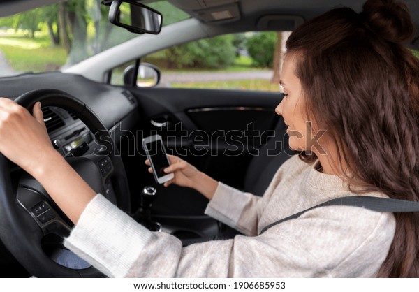 safety and people\
concept - happy smiling young woman or female driver with\
smartphone driving car in\
city