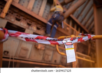 Safety Prevention Red And White Danger Tape And Tag Are Barriers On Exclusion Dropped Object Zone While Defocused Construction Abseiler Working In Fall Arrest, Fall Restraint At The Background 