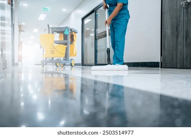 A Safety sign with caution phrase. Happy young housekeeper mopping the floor with a mop and cleaning products to clean dust in a hospital corridor.