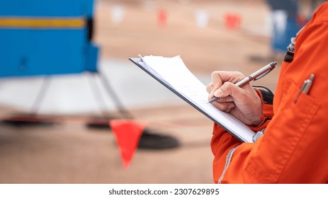 A safety supervisor is handwriting on paper for take note some finding during perform safety audit at construction worksite. Industrial working action with people part, selective focus.