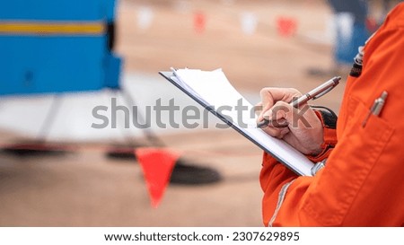 A safety supervisor is handwriting on paper for take note some finding during perform safety audit at construction worksite. Industrial working action with people part, selective focus.