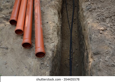 Safety supply to house new insulated internet, gas cord, red metal-plastic tap system construction lay in pit dug in garden. Top view with space for text on grey clay earth. Telecom service industry