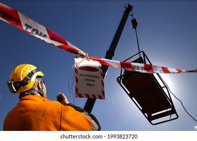 Safety Work Practice Red And White Warning Danger Tag Tape Sign Applying On Exclusion Dropped Zone Where Rigger Operating 2 Way Radio With Crane Operator During Lifting Heavy Load At Open Field 