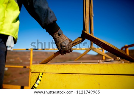 Safety work practices construction worker crane rigger wearing heavy duty glove holding safety control a two tones yellow lifting sling which its connecting to the load while crane is lifting 