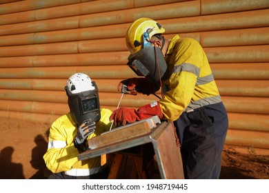 Safety workplace welder wearing dark safety shield mask eyes protection welding leather glove welding chute liners repairing while supervisor is guiding inspecting by his side Australia mining site