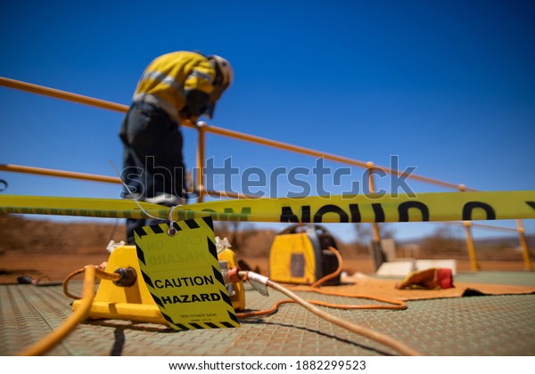 Safety workplace yellow striped caution tape warning\
sign barricade exclusion zone preventing from public access while\
defocused construction worker welder welding repairing fence    \
