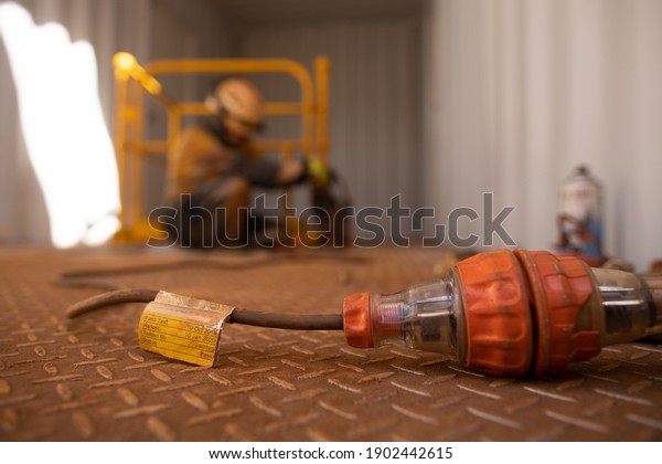 Safety workplaces approved pass test tag of\
electrical device attached on power cord while defocused worker\
using power drill on construction site\
