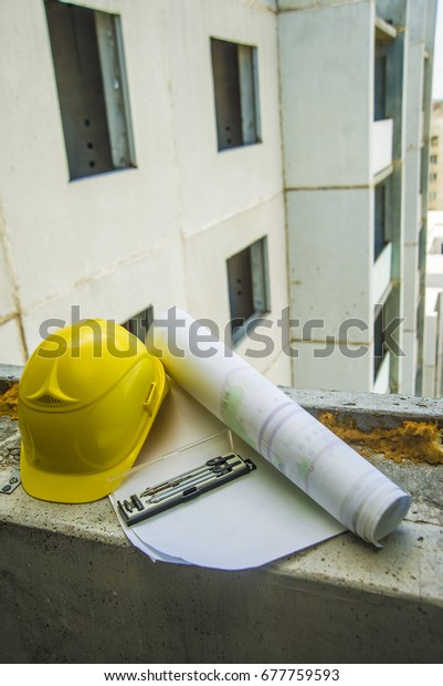 safety yellow\
helmet blue print plan, compass and construction equipment on\
engineer working table with building construction background use\
for real estate and land development\
theme