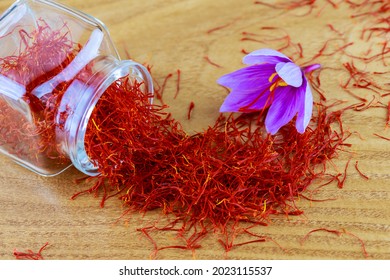 Saffron stigmas scattered on a wooden surface from a glass bottle. Flowering saffron sativus. Saffron crocus flowers