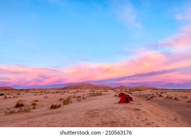 Sahara Desert camp at sunrise with a row of red tents in the sand. Adventure travel concept. Copy space for text.