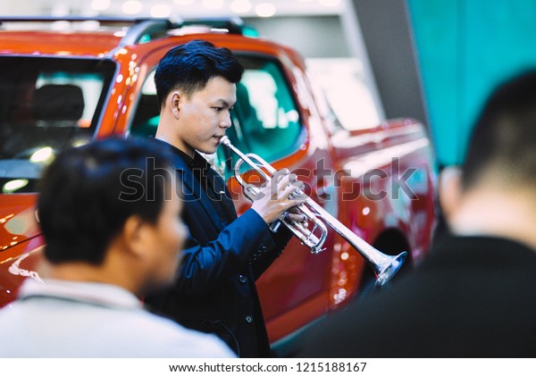 SAIGON EXHIBITION AND CONVENTION CENTER (SECC), HO\
CHI MINH CITY, VIETNAM - OCTOBER 2018: Unidentified man are playing\
trumpet at Vietnam Motorshow 2018 event with background of the red\
car
