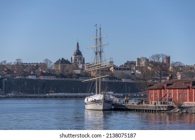 Sail boat, the brig Tre Kronor af Stockholm at a jetty on the island Kastellholmen and the district Södermalm with church and towers a sunny spring day in Stockholm, Sweden 2022-03-20