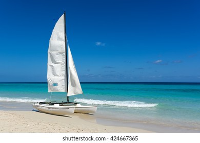 Sail Boat, Catamaran, On Tropical Beach With Blue Water Background