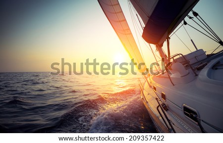 Sail boat gliding in open sea at sunset