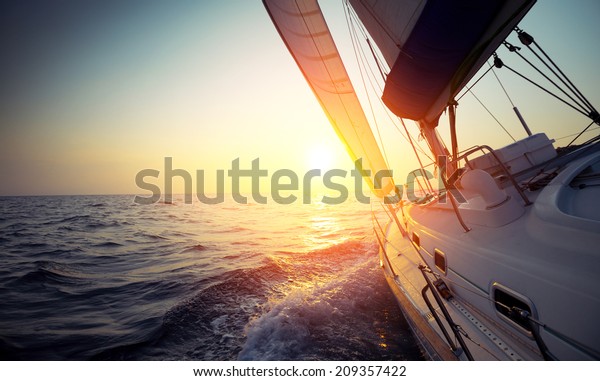 Sail boat gliding in\
open sea at sunset