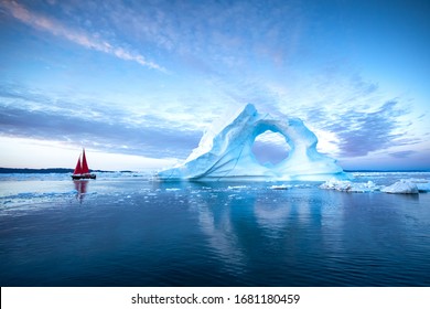 Sail boat with red sails cruising among massive ice bergs during dusk. Disko Bay, Greenland. - Shutterstock ID 1681180459