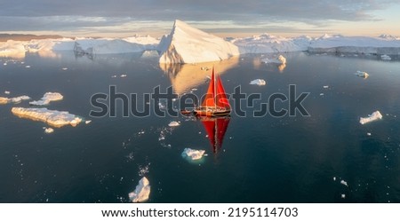 Sail boat with red sails cruising among ice bergs during sunset. Disko Bay, Greenland.
Midnight sun, romantic view.
Climate change and global warming
