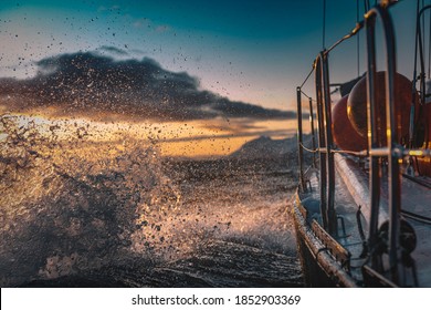 Sail Boat Sailing Through Rough Sea Water With Waves Splashes, Side View With Snowy Mountains On Background