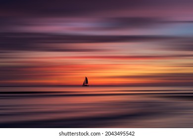 A sail boat at sea with a stunning tropical sunset and waves coming to the beach. Motion blur background and foreground for a dreamy silky effect