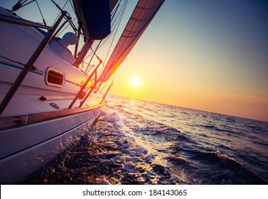 Sail boat with set up sails gliding in open sea at sunset