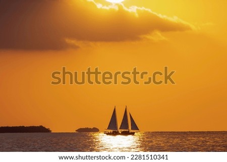 A sail boat is shadowed during the golden hour of sunset on the water off Key West Florida. 
