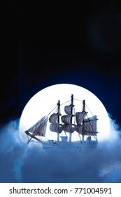 Sail ship in light of full moon. Wooden model on dark background. Conceptual marine still life.