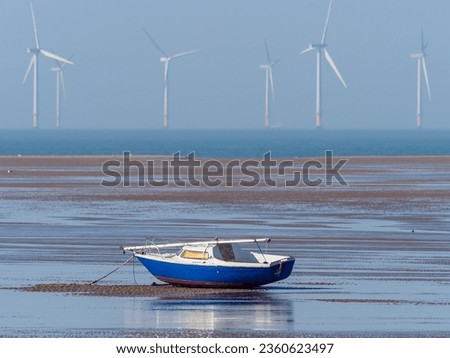sailboat aground at low tide with energy producing wind turbines in the distance