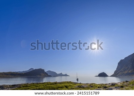 A sailboat basking in the sun's radiance on the serene waters near Haukland Beach in the Lofoten Islands, under a vast clear sky. Norway