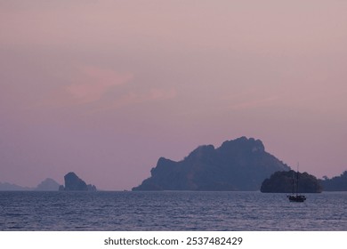 A sailboat gently glides through calm waters at twilight, surrounded by distant islands silhouetted against a stunning sunset, creating a tranquil atmosphere. - Powered by Shutterstock